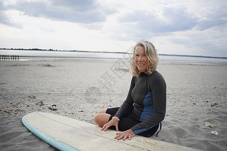 海滩上坐在冲浪板旁边的中年女性肖像图片