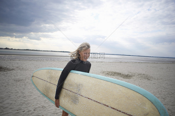 中年妇女从海边步行携带冲浪板图片