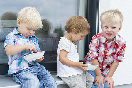 女幼儿和两个坐在院子里的年轻兄弟吃着一碗草莓图片