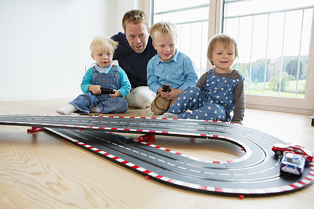 在客厅地板上玩具赛车的中年男子和3名中幼儿图片