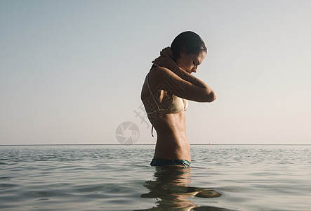 美丽的年轻女人手放在海中脖子后图片