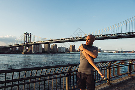 美国纽约曼哈顿大桥前伸展的年轻男跑步者图片