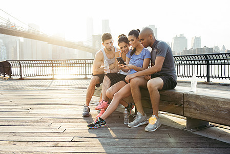 四位成年跑友在美国纽约布鲁克林桥前阅读智能手机文字图片