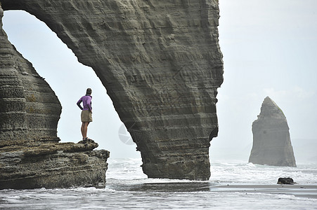 在新西兰北岛海滩岩层上站立的年轻妇女图片