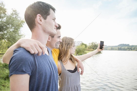 青年朋友在湖边使用智能手机自拍图片
