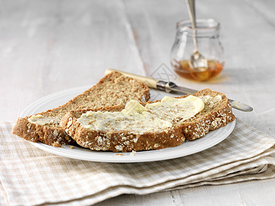 用黄油刀和蜂蜜涂抹在全餐面包上图片