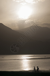 尼泊尔骑自行车的人在日落时观看山和湖的剪影图片
