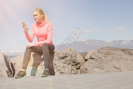一个穿着运动服的少女坐在岩石上看手机图片