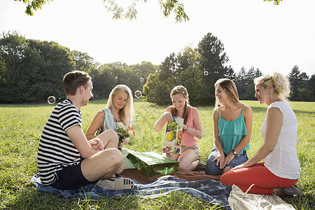青年男女坐在公园的野餐毯子上互送礼物图片