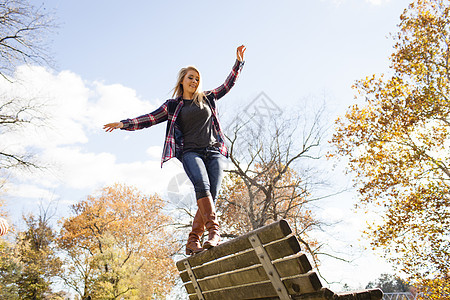 在秋林公园长椅上保持平衡的年轻女子图片