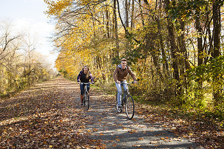 二人在铺满落叶的道路上骑行图片