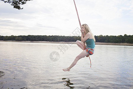 年轻女子抓着在湖上的绳摇摆图片