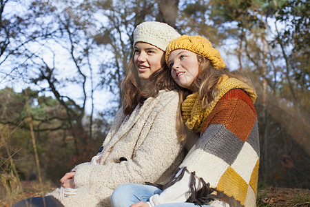 年轻女孩穿着毛衣在森林中并肩坐在一起微笑图片