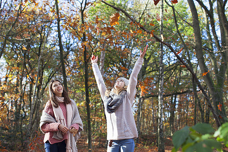 年轻女孩在森林中微笑着举起秋叶图片