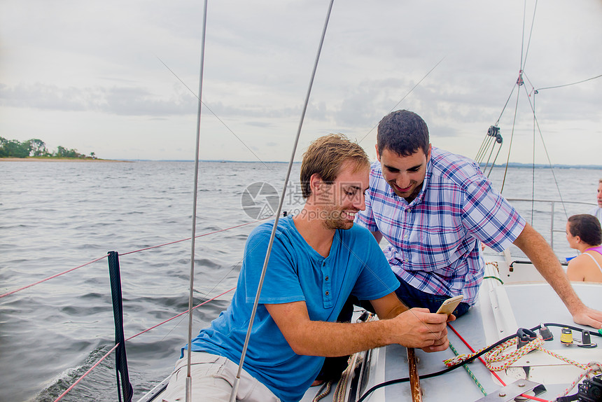 乘帆船上的男子看着手机微笑图片