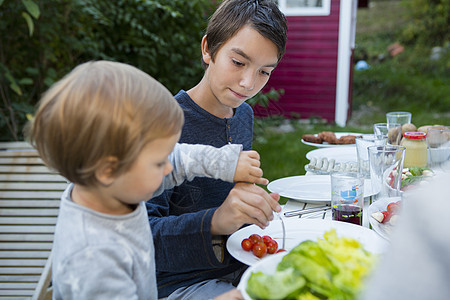 帮助女幼儿在花园烧烤时吃食物的少年男孩图片