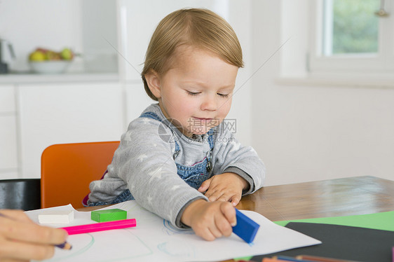在厨房桌边绘画时使用抹布的女幼儿图片