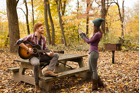 在秋林中的年轻女子拍摄男朋友弹吉他图片