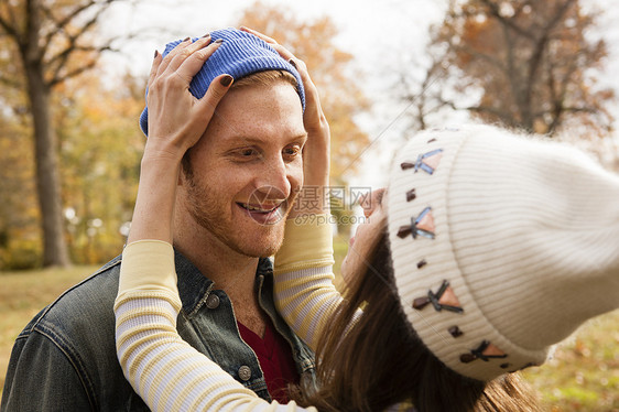 在公园浪漫的年轻女性调整男朋友的帽子图片
