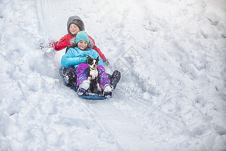 在雪覆盖山坡上滑雪的兄妹和狗狗图片