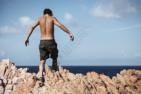 身穿卡其短裤的赤胸青年男子爬过岩石图片