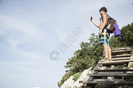 年轻人站在木制阶梯上用智能手机拍照的侧视图图片