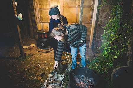 一对夫妇微笑着用夹子从火中取出粘土锅图片