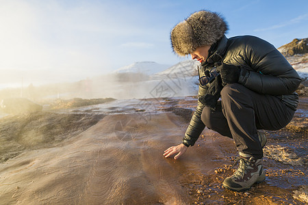 冰岛西南部Laugarfjall山山坡上的Haukadalur山谷中的一个大间歇泉旁的一名妇女正在触摸地面图片