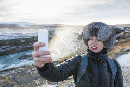 在位于冰岛西南部Hvita河峡谷的Gullfos瀑布上自画像的妇女图片