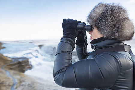 妇女使用望远镜查看位于冰岛西南Hvita河峡谷的Gullfos瀑布图片