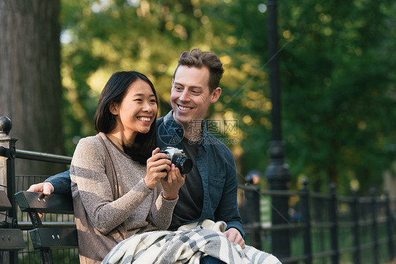 拿着相机的女人和男友坐在长椅上图片