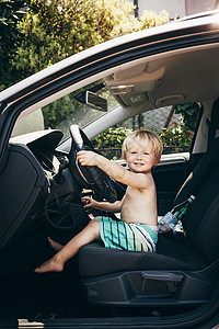 坐在驾驶座上手扶方向盘假装开车的小男孩图片