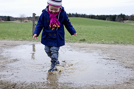 穿着橡皮靴在水坑中踩水的小女孩图片