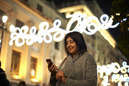 在街道装饰灯前使用智能手机的妇女图片