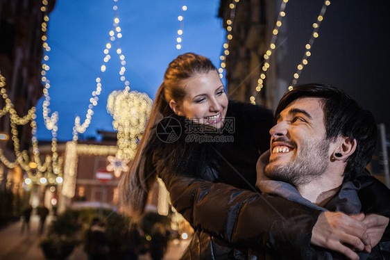夜晚街上年轻男子背着年轻女子对视微笑图片