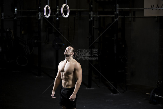 准备在黑暗体操场使用健身环的赤胸青年男子图片