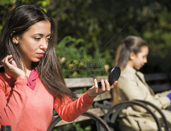 坐在公园长椅上看着镜子的年轻女士图片