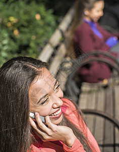 坐在公园长椅上闲聊智能手机的年轻女子图片