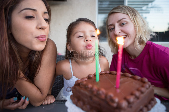 和家人坐在一起的年轻女孩在生日蛋糕上吹蜡烛图片
