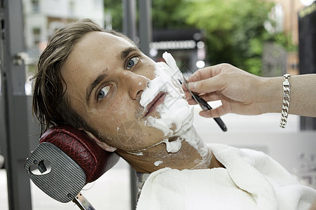 理发店的年轻人脸被剃须膏遮住脸被剃须刀光图片