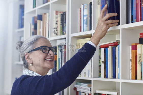 快乐的灰色头发成年女人从书架上挑选本图片