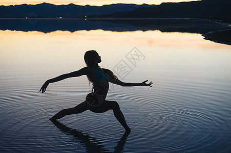 日落时分美国犹他州博纳维尔盐滩湖中一位女舞者的剪影张开双臂图片