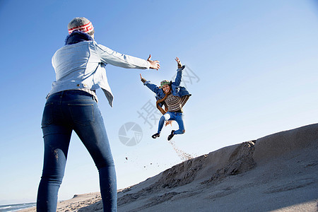 年轻女孩看着朋友跳上沙丘图片