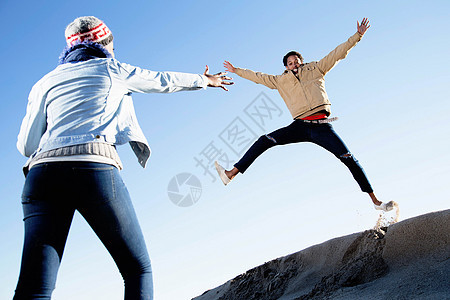 冬天在海滩上玩耍的年轻夫妇人跳跃图片