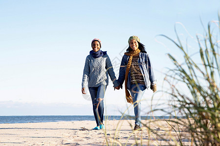 两个年轻女子在海滩上散步手牵微笑图片