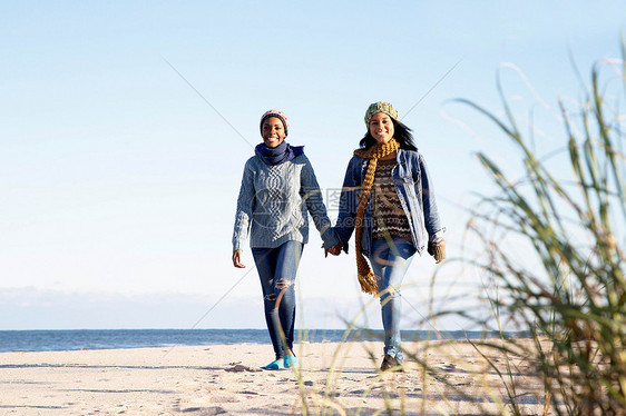 两个年轻女子在海滩上散步手牵微笑图片