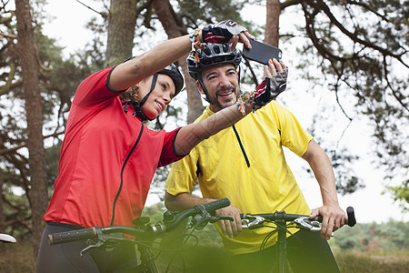 在森林里骑智能手机自拍的山上骑行车的情侣快乐图片