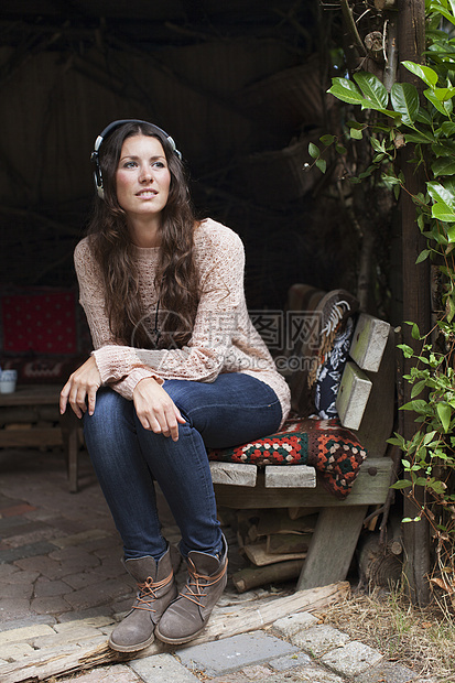 坐在花园门廊旁听耳机音乐的年轻妇女图片