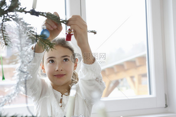 女孩举起手臂在圣诞树上增加装饰图片