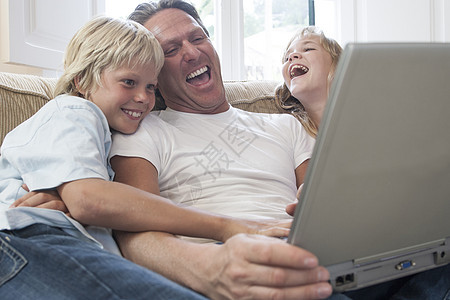 父亲和儿童笑在客厅使用笔记本电脑图片